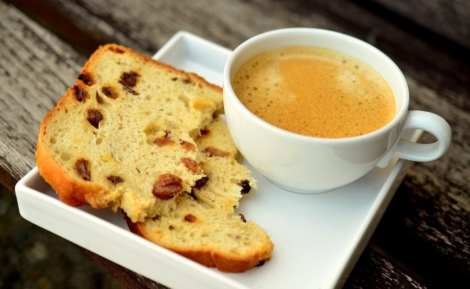 Kahvikuppi, jossa kahvia ja lautasella leipä.