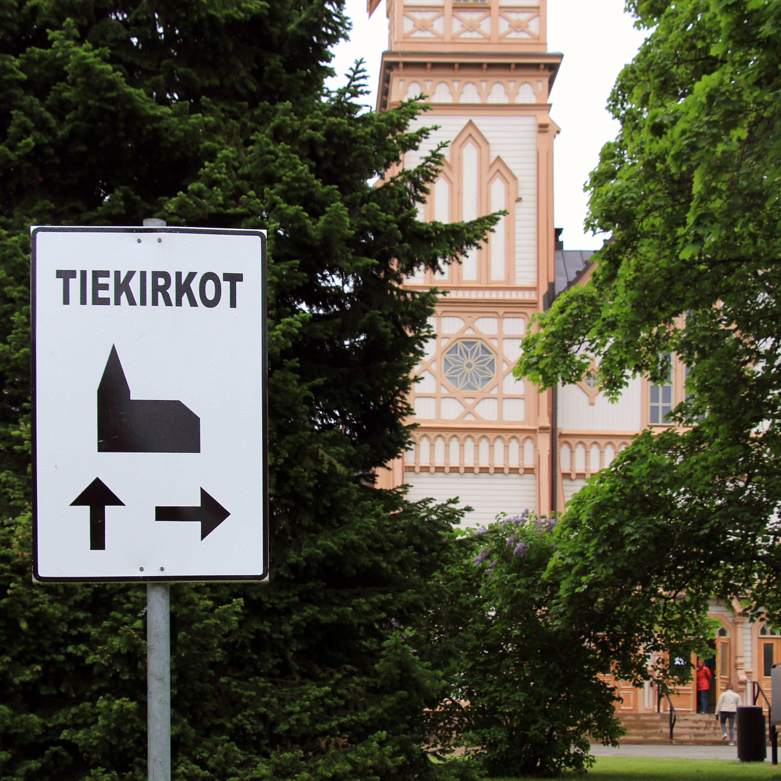 Tiekirkkoon ohjaava opastemerkki, taustalla vierailijoita menossa Kajaanin kirkkoon