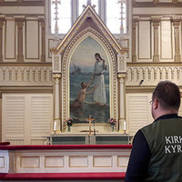 Kajaanin kirkon alttarin edessä seisoo pappi, yllään vihreä liivi, jonka selässä lukee kirkko, kyrkan.